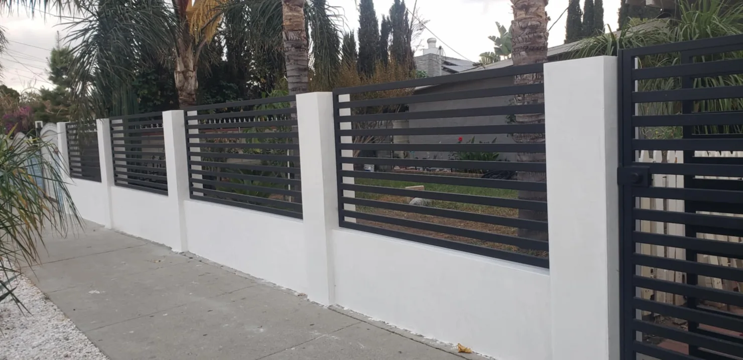 A white wall with black fence and a tree in the background.